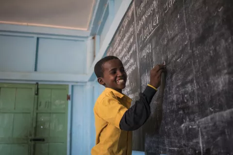 A student laughs as he writes the answers to questions on the chalkboard of his classroom.